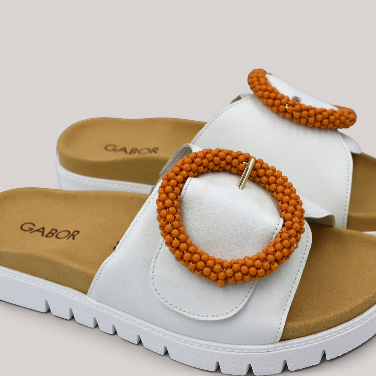 Grundy's Shoes Gabor white leather slide sandals with a tan contoured footbed and oversized orange beaded buckle.
